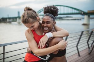 Zwei Frauen in Sportklamotten lachen und nehmen sich in den Arm.